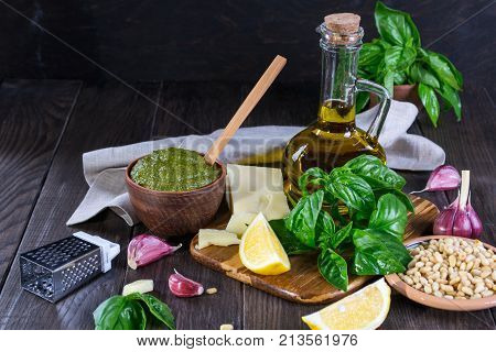 Tradizione Italiana Homemade Pesto recipe ingredients on dark table. Parmesan cheese basil leaves pine nuts olive oil garlic.