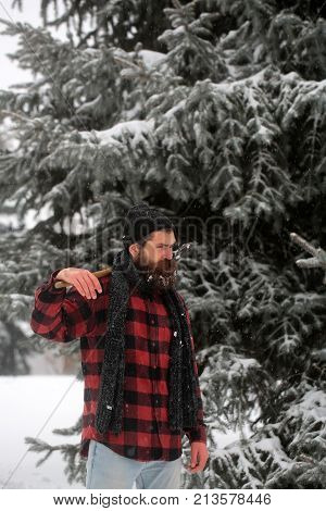 Christmas hipster lumberjack with ax in wood.. Man with beard in winter forest with snow hold axe. Wanderlust hiking and travel. New year man in snowy cold forest. Winter holiday and celebration.
