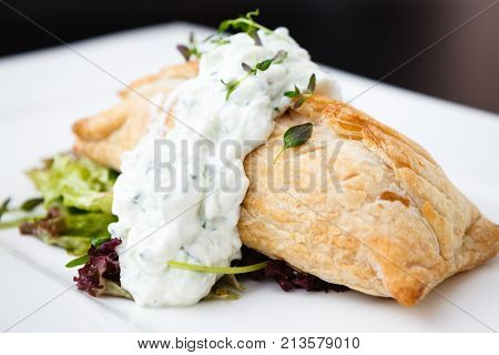 Traditional russian pie - coulibiac. Baked puff pastry filled with smoked salmon, served with sour cream sauce