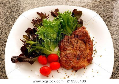 Roasted meat steak with green salad on dark stone background, top view