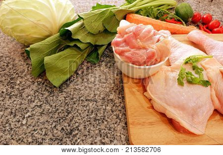 Sliced raw chicken on wood cutting board with vegetable on black stone background