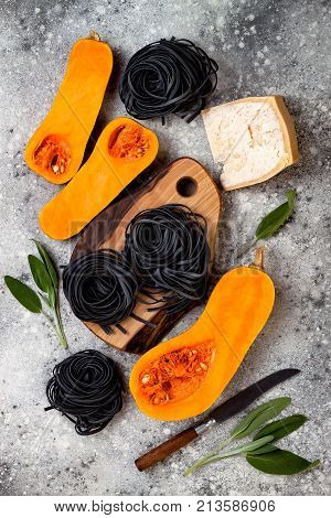 Raw ingredients for making black pasta with butternut squash parmesan cheese and sage. Concrete background top view flat lay. Halloween black and orange party dinner concept