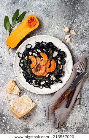 Black pasta with roasted butternut squash parmesan cheese and fried sage. Concrete background top view flat lay. Halloween black and orange party dinner concept