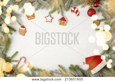 Table top shot of a frame made of fir branches decorated with gingerbread cookies and sweets with christmas lights in the foregorund
