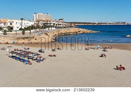 Orihuela Spain - November 5 2017: People sunbathing at the Cala Capitan beach in the Cabo Roig popular place for holidaymakers. Province of Alicante. Costa Blanca. Spain