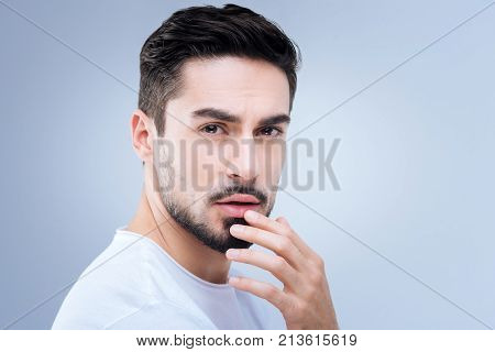 Tender touch. Romantic pleasant sensitive man looking emotional while touching his lips and thinking about a sweet kiss of his beloved woman