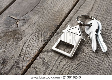 Two steel keys with house shaped trinklet on keyring on wooden background with copy space. Home key, safety, security, real estate and rent concept
