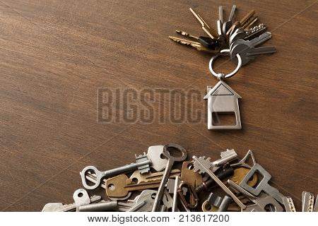 Bunch of keys with house shaped trinklet against wooden background and collection of different keys. Safety, security and real estate concept, top view, copy space
