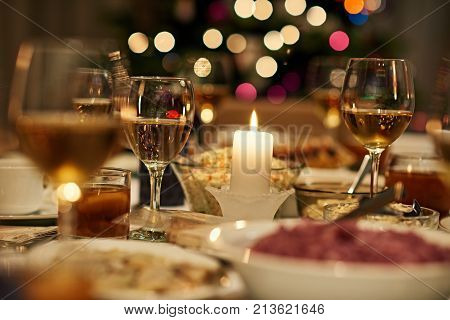 Beautiful dining table full of a variety of delicious festive food and wine with a Christmas tree in the background in candle ight mood