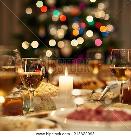 Beautiful dining table full of a variety of delicious festive food and wine with a Christmas tree in the background in warm mood