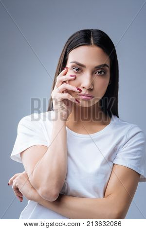 Nail designer. Calm beautiful nail designer standing against the blue background with her fingers touching her right chick while waiting for the clients to visit her