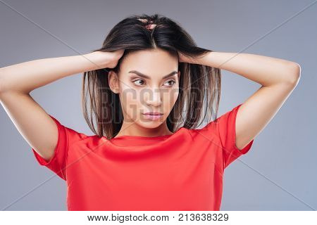 Unpleasant hair. Calm serious woman being not satisfied with her new shampoo while touching her unpleasant hair and looking into the distance