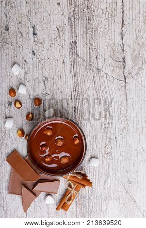 A bowl of melted milk chocolate with hazelnuts randos marshmallow, cinnamon, and hazelnuts. View from above