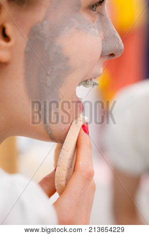 Woman Removing Mud Facial Mask With Sponge