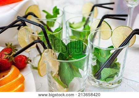 Fresh fruits and berries of different bright colors cut in small pieces are served on a table with mohito cocktail
