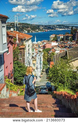 ISTANBUL TURKEY: Beautiful girl standing on a stair in Kuzguncuk district with view of Bosphorus and Bosphorus Bridge on background on October 10 2017