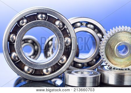 Group of various ball bearings and gears close up on nice blue background with reflections.