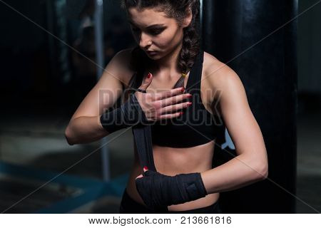 Sad Young fighter boxer girl putting on hand bandage before training with heavy punching bag. She looks down