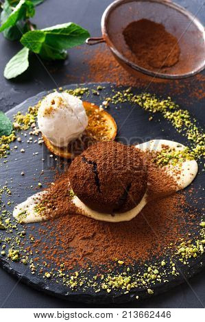 Exquisite french dessert. Chocolate fondant with creme anglaise and vanilla ice cream, sprinkled with cocoa, served on round slate finely decorated with orange citron and pistachio crumble, closeup