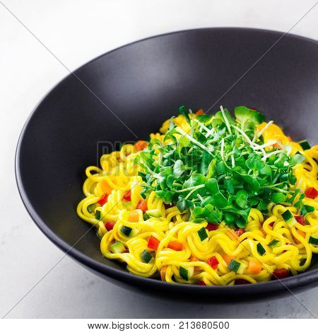 noodles with microgreens and vegetables in a black plate
