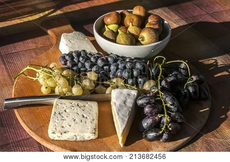 Wooden plateau with fresh grapes figs and types of cheese closeup as homefood background