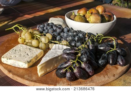 Wooden plateau with fresh grapes figs and types of cheese closeup as homefood background