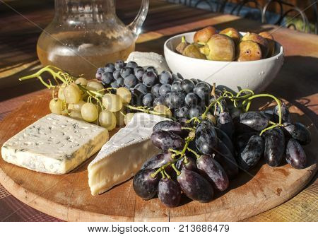 Wooden plateau with fresh grapes figs and types of cheese closeup as homefood background