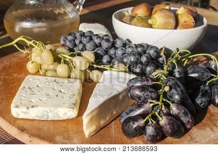 Wooden plateau with fresh grapes figs and types of cheese closeup as homefood background