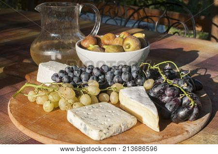 Wooden plateau with fresh grapes figs and types of cheese closeup as homefood background