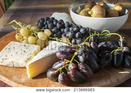Wooden plateau with fresh grapes figs and types of cheese closeup as homefood background