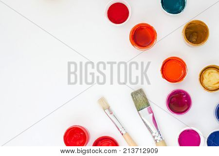 Set Of Brightly Colored Paints With Brushes On White Table Backround Top View.