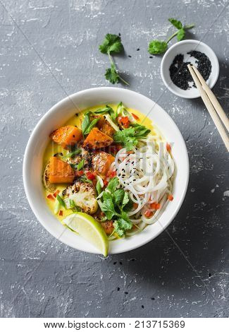 Vegan khao soi soup on a grey background top view. Vegetarian soup with turmeric rice noodles baked pumpkin and cauliflower. Healthy food concept