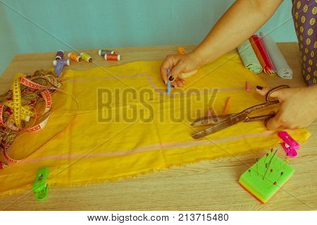 Close up of woman's hands drawing a pattern on yellow tissue. Measuring tape and sewing accessories. A tailor is laying out a dress/Sewing layout - Retro color