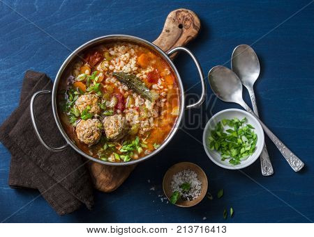 Multi grain meatballs and vegetables soup in a pot on a blue background top view. Comfort home cooking healthy seasonal food concept