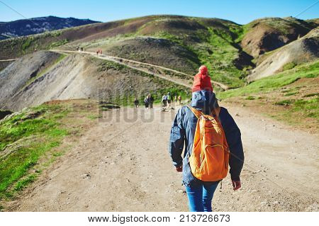back view of woman traveler with small orange backpack on a walk in the Valley of the river of Hveragerdi Iceland. Hiking Tour of Reykjadalur Hot Springs