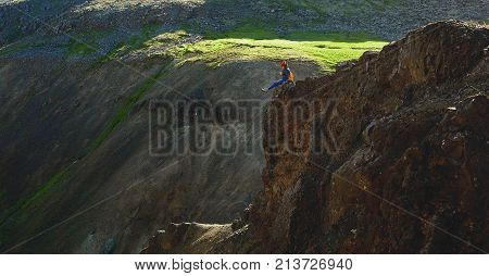 back view of woman traveler on a walk in the Valley of the river of Hveragerdi Iceland. Hiking Tour of Reykjadalur Hot Springs. woman sits on the cliff and looks at the sun