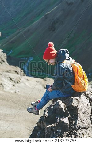 back view of woman traveler on a walk in the Valley of the river of Hveragerdi Iceland. Hiking Tour of Reykjadalur Hot Springs. woman sits on the cliff and use smartphone