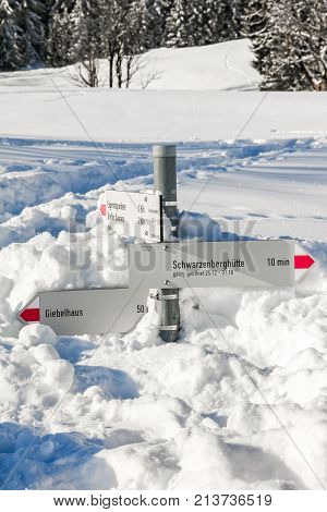 Hiking trail signpost sticks out of deep snow. Mountains winter landscape on sunny day. Allgau, Bavaria, Germany.