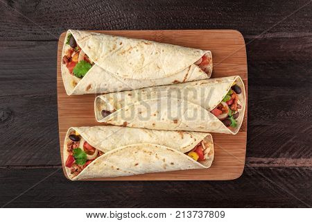 An overhead photo of Mexican burritos with beef, rice, black beans, vegetables, and chili peppers, with a place for text, shot from above on dark wooden rustic textures