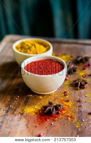 Close up two bowls filled with red paprika and yellow turmeric powder on dark wooden table covered with anise