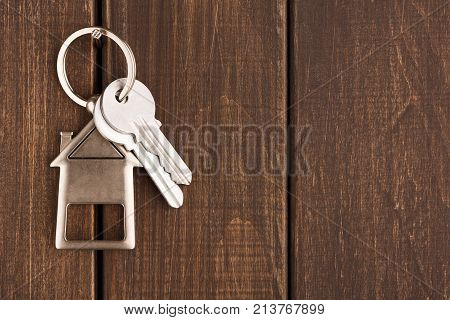 Two steel keys with house shaped trinklet on keyring on brown rustic wooden background with copy space. Home key, safety, security, real estate and rent concept, top view