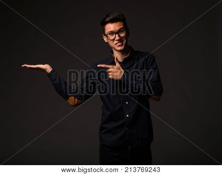 Young jocular man portrait of a confident businessman showing by hands on a black background. Ideal for banners, registration forms, presentation, landings, presenting concept.
