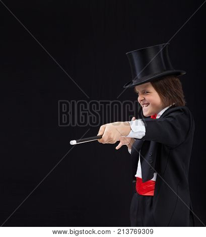 Magician boy with hardhat pointing to copy space with magic wand and making evil grimace with a grin