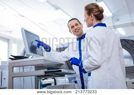 Strong team. Couple of researchers discussing interesting medical case while he pointing at the screen and smiling to her