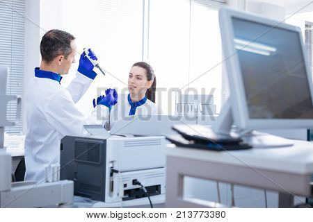 Be attentive. Experienced  laboratorian holding the medical marker and showing the procedure of analyzing to naive young colleague while standing in the lab