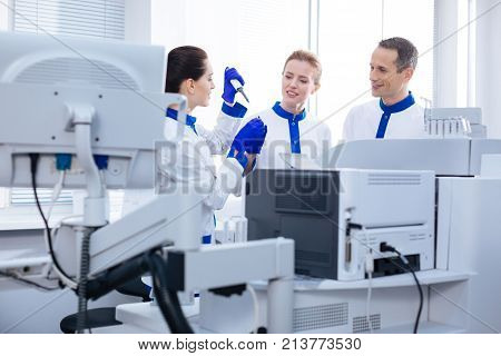 Well done. Two charming intelligent laboratorians checking how intern coping with conducting  analyzes while standing behind the medical equipment