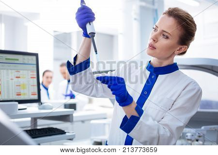 Blood test. Experienced appealing female laboratorian measuring liquid while scrutinizing and posing in the lab