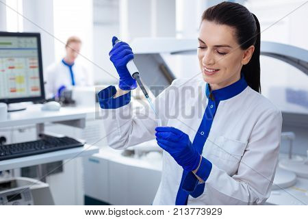 Be precise. Young promising attractive intern  carrying a glassware where she putting a drop of chemicals while posing in the lab