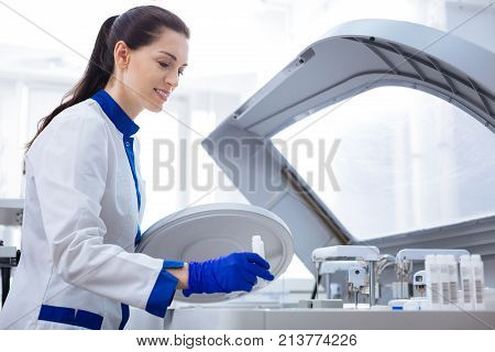 Blood separation. Professional focused laboratory assistant looking down holding lid and preparing to place special container