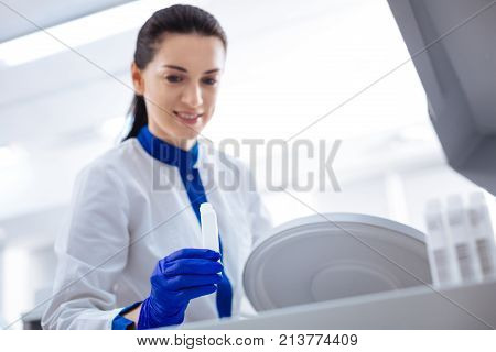 Start working. Selective focus of white medical container hold by brunette  enthuasiastic female laboratory assistant who wearing labcoat and smiling